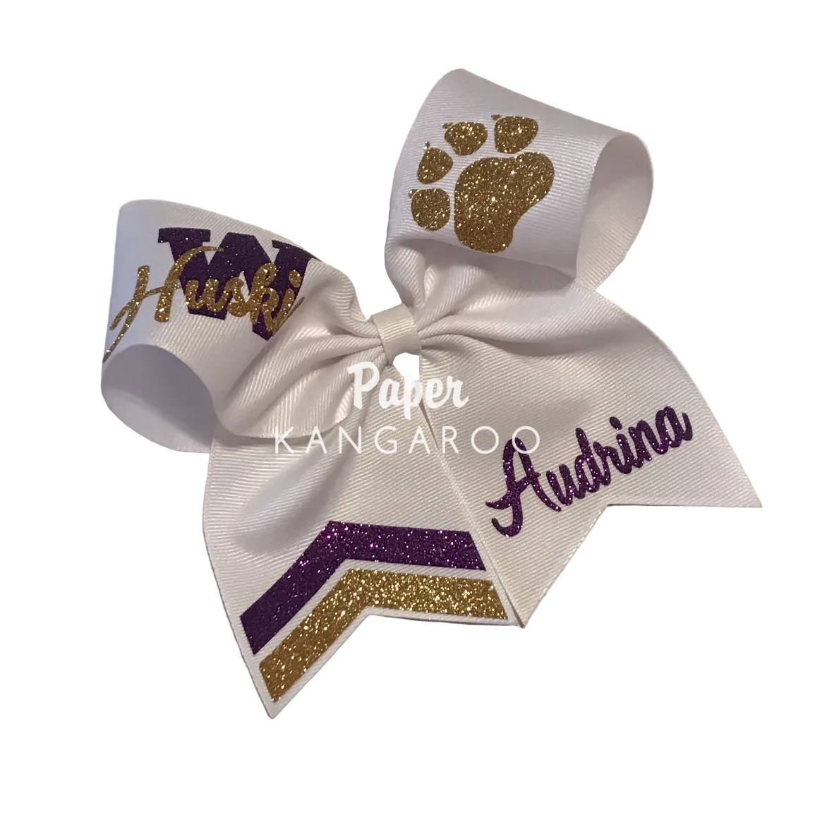 A custom white cheerleader hair bow with purple and gold glitter accents, featuring a paw print, a 'M' monogram, the name 'Audrina' in purple script, and chevron stripes. A watermark reading 'Paper Kangaroo' is overlaid in the center.