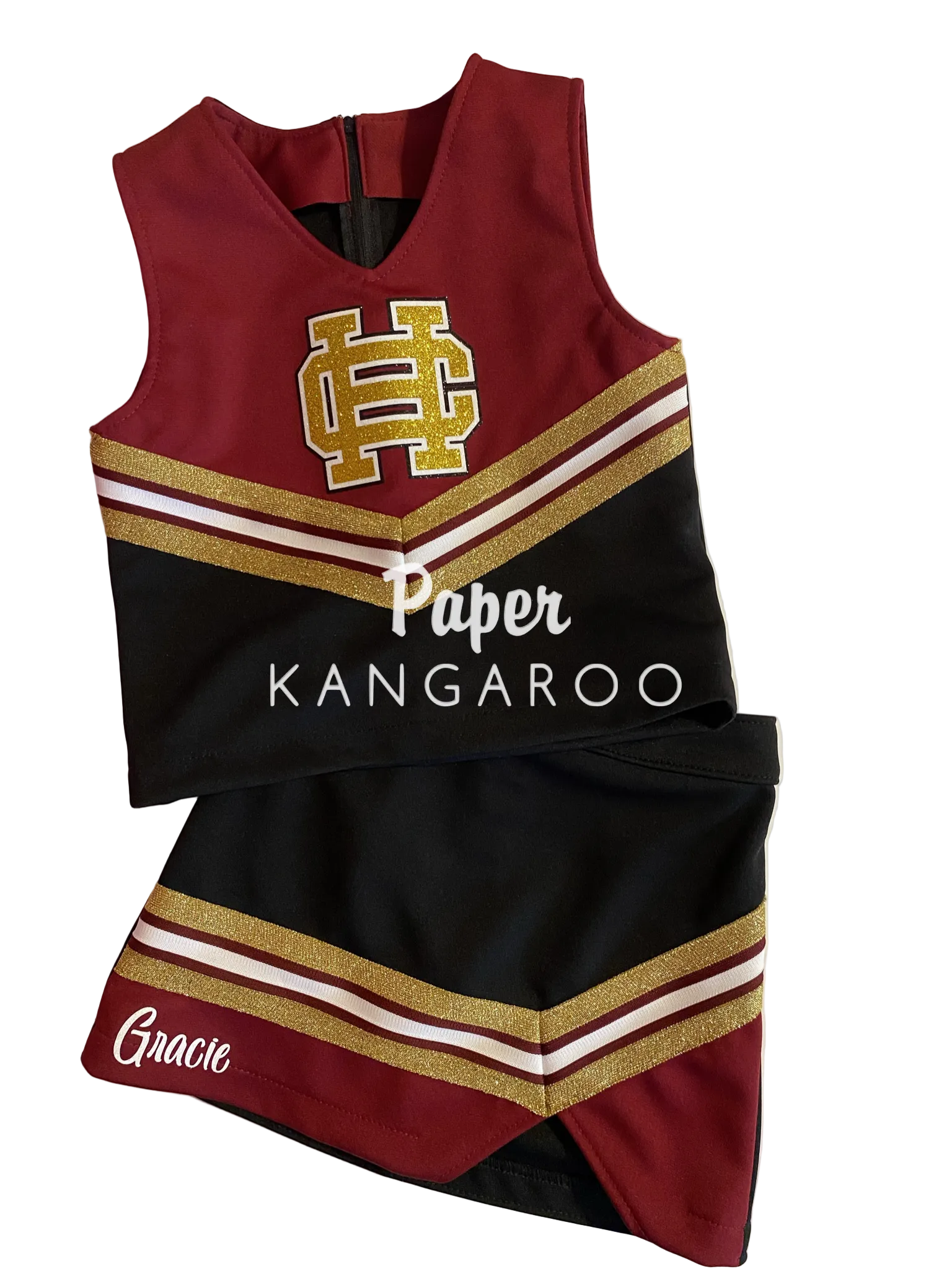 A cheerleader-style sleeveless top and matching skirt set laid flat on a white board. The outfit is primarily deep burgundy and black with gold glitter-style stripes and white trim.