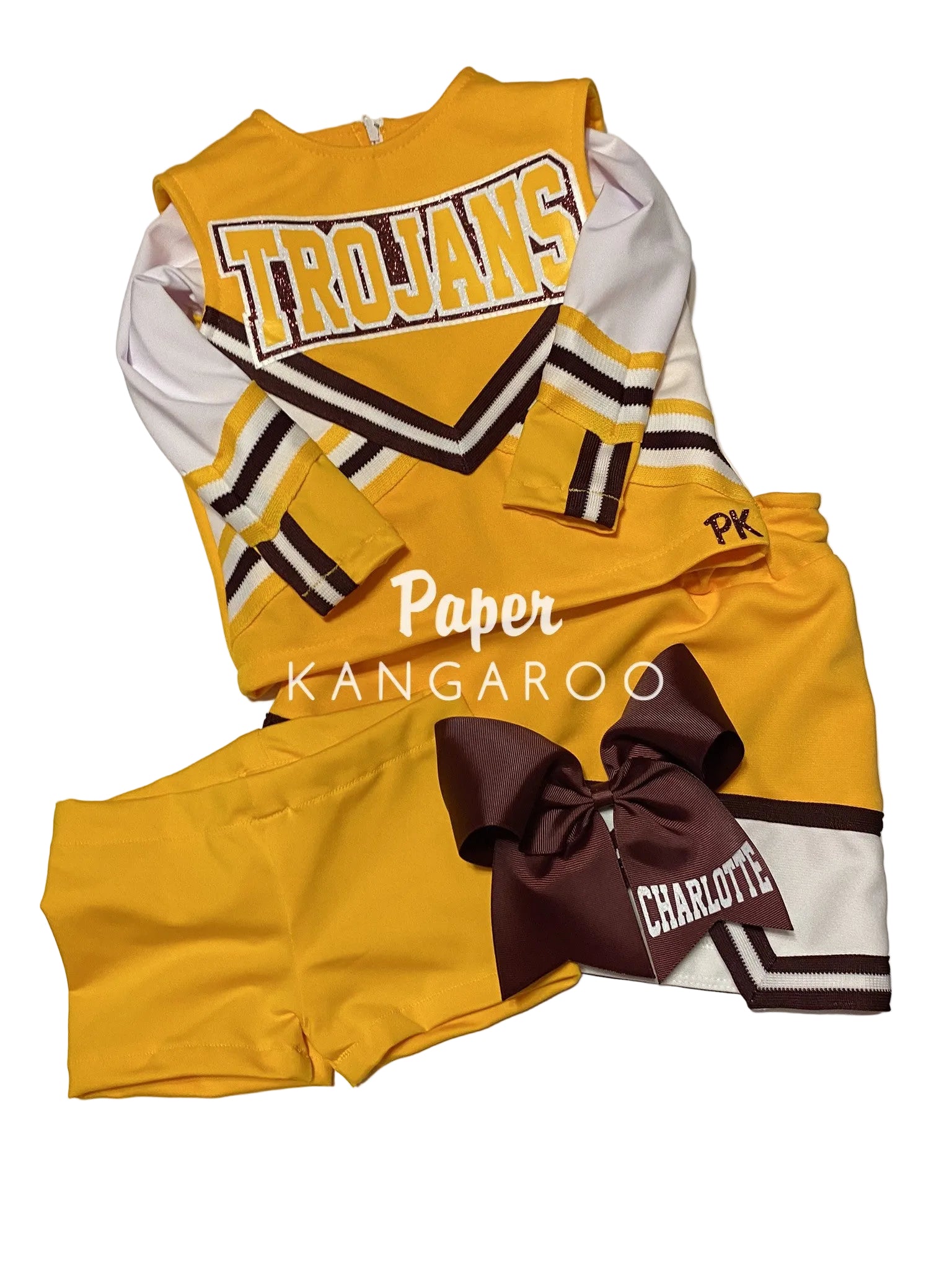 A yellow and white cheerleader-style outfit set laid flat on a white surface, including a long-sleeve jersey with 'TROJANS' across the chest, matching shorts, and a large dark brown bow with 'CHARLOTTE' text. A watermark reading 'Paper Kangaroo' is overlaid on the center.