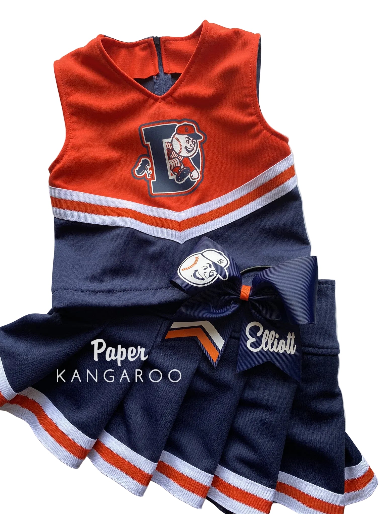 A custom children's cheerleader dress set with a navy blue skirt, orange and navy top, and matching bow. Features custom text 'Paper KANGAROO' and 'Elliott' on the skirt, along with a custom mascot logo.