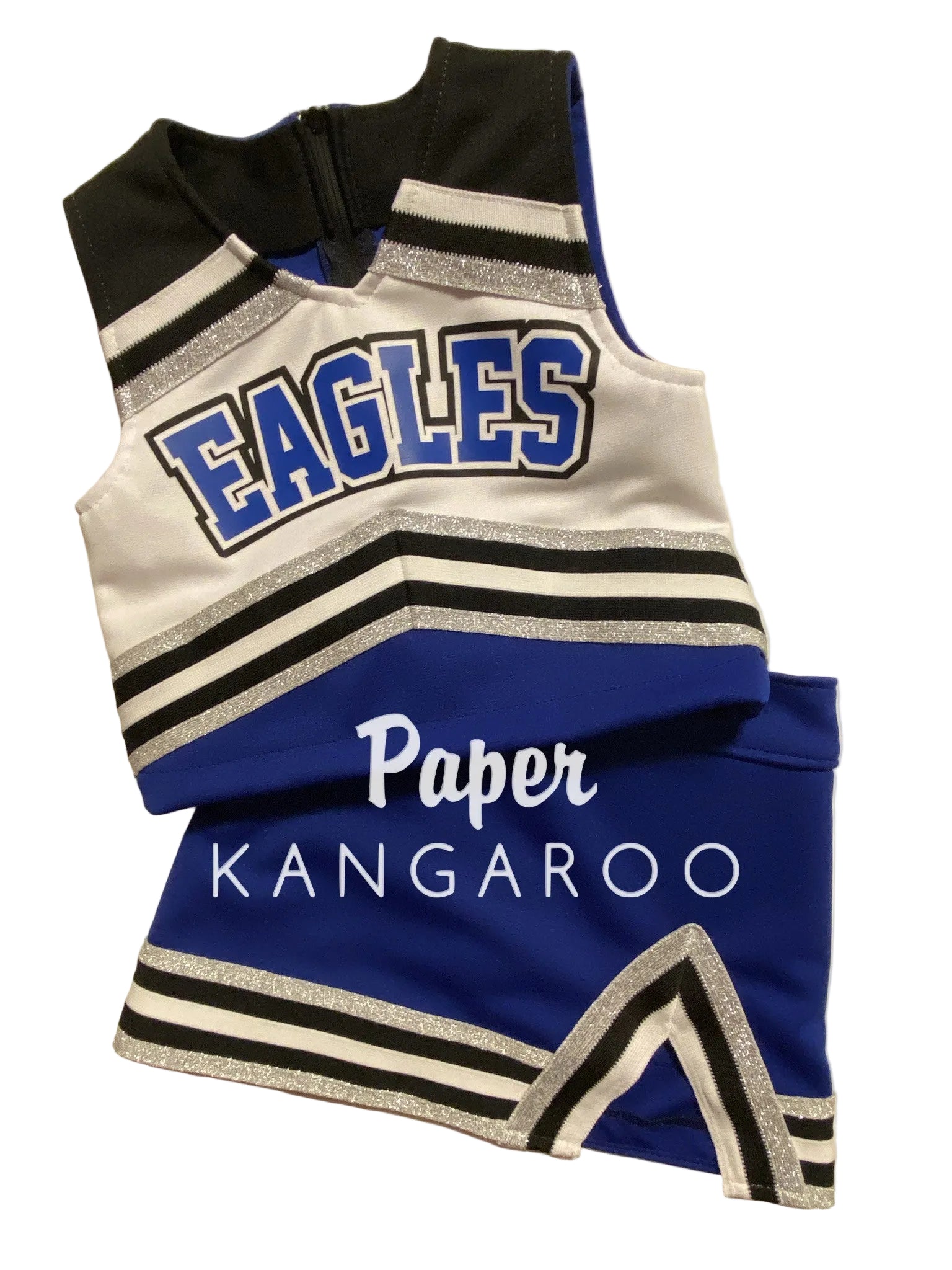 A cheerleader-style two-piece outfit laid flat on a light beige background. The sleeveless top is white with black and silver glitter stripes, black shoulder panels, and large blue 'EAGLES' lettering outlined in white.