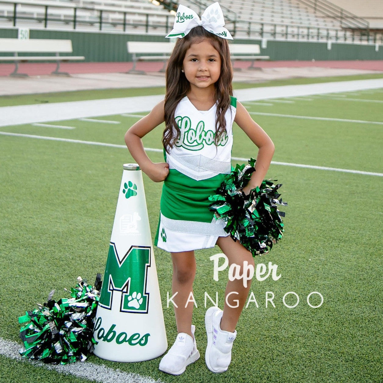 Young cheerleader smiling on a football field wearing a kelly green and white Loboes uniform with a paw print skirt detail, holding green, black, and white pompoms beside a white megaphone.