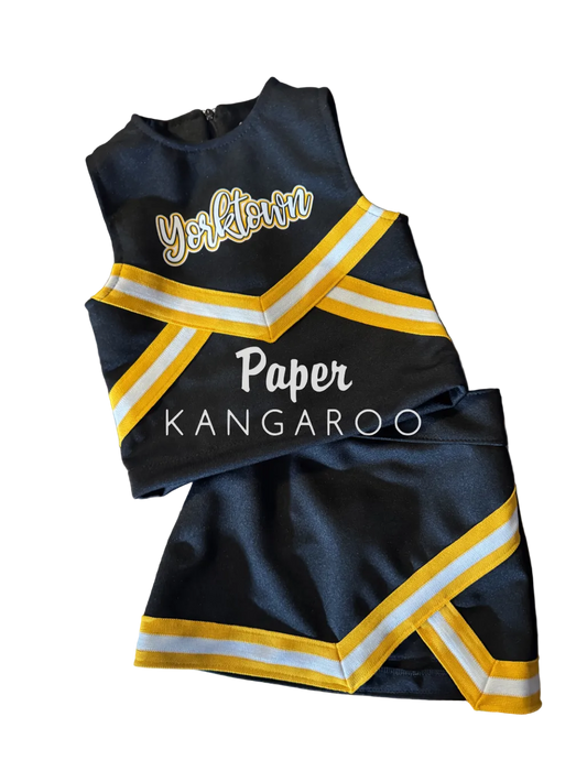 A custom cheerleader outfit set consisting of a black top and matching shorts with yellow and white striped trim, laid flat on a wooden table. The top features 'Yorktown' in white script with a gold outline, and the bottom features 'Paper KANGAROO' in white text.
